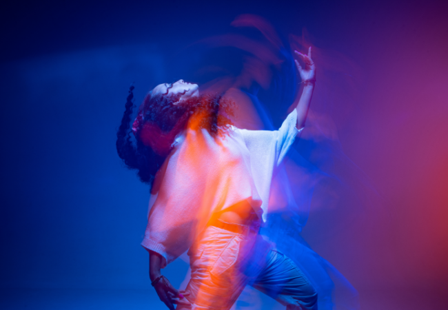 Cool dancing young mixed race girl in colorful neon studio light. Long exposure. Contemporary hip hop dance, rap rhythm.