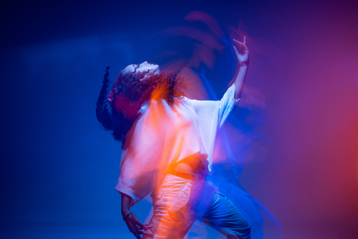 Cool dancing young mixed race girl in colorful neon studio light. Long exposure. Contemporary hip hop dance, rap rhythm.