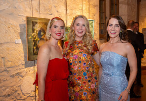 3 females posing for a photo in front of hanging artwork.